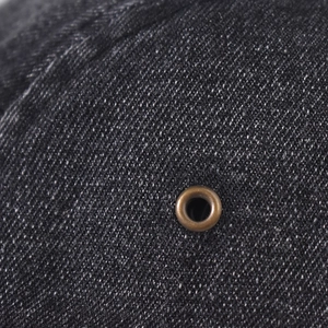 Close-up detail of dark grey washed denim fabric with a bronze metal eyelet on the cap