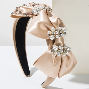 Détail du serre-tête en satin champagne avec nœuds, perles et cristaux brillants