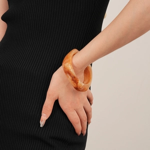 Detail eines Bernstein-Resin-Armreifs mit Marmormuster auf schwarzem Strickärmel