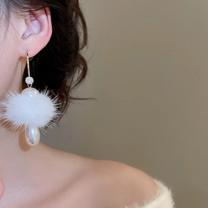 Detail of elegant C-shaped silver earrings with fur pompom and pearl drop on model