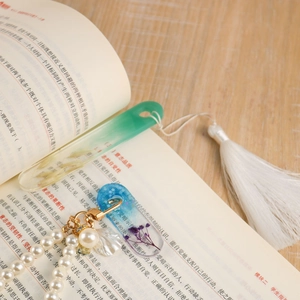 Handmade resin bookmarks with dried flowers and tassels displayed on an open book