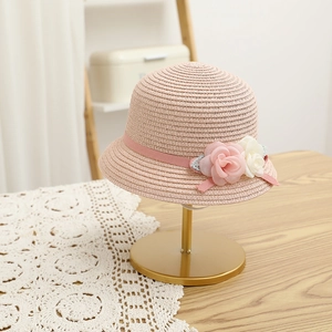 Close-up of pink straw sun hat with delicate ribbon and fabric roses on a metal stand