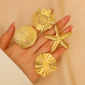 Close-up of four chunky gold flower and starfish open rings on a model's hand
