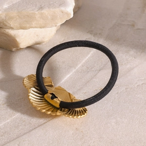 Elastic hair tie in black with golden seashell and scallop metal accents on stone background