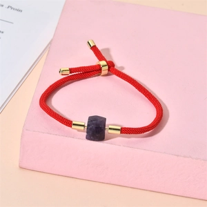 Détail du bracelet en corde tressée rouge avec cristal hexagonal violet et perles dorées