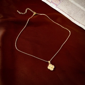 Détail d'un collier pendentif trèfle doré avec micro-diamants sur un fond en velours rouge