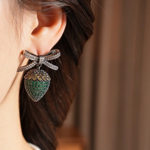 Close-up of vintage bow and strawberry earrings with zircons on a female model
