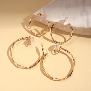 Chic gold twisted geometric clip-on earrings in two sizes on minimalist marble background