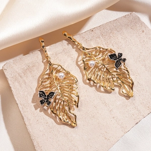 Detailed view of gold leaf earrings with black butterfly and white pearl accents on silk