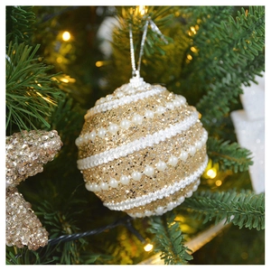 Detail of champagne gold sequined Christmas ball with pearl stripes on green tree
