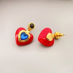 Macro detail of heart-shaped earring with red resin, blue gem, and gold-plated edges