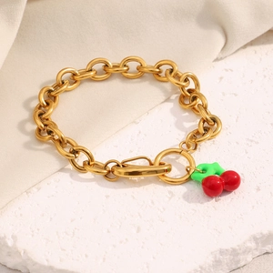 Detail of 18K gold plated chain bracelet with red and green cherry pendant on stone texture