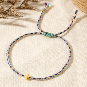Detail of a handmade woven bracelet with golden cross charm and adjustable purple string