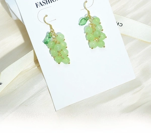 Detail view of grape-shaped beaded earrings with green leaves on a white card