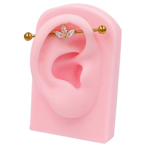 Gros plan du piercing industriel doré avec trois zircons marquise sur modèle d'oreille