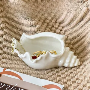 Ceramic conch jewelry tray with white glossy finish on a textured beige background