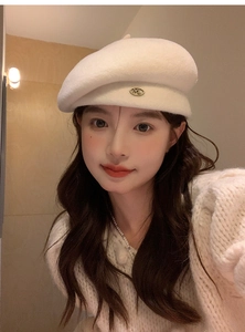 Close-up of white wool beret featuring a metallic ML letter logo and soft felt texture