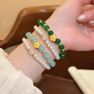 Detalle de pulseras de cuentas apilables con piedras naturales y dijes de flores de oro.