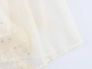 Détail du tissu en tulle beige avec broderie florale et paillettes sur la robe