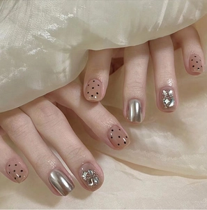 Close-up of nude press-on nails with silver mirror finish, dots, and sparkling rhinestones