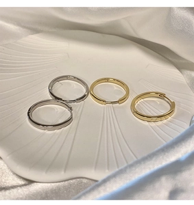 Vista dall'alto di orecchini a cerchio oro e argento su ceramica bianca e seta