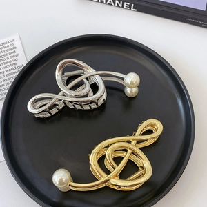 Elegant gold and silver music note hair clips with white pearls on a sleek black tray