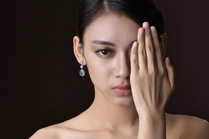 Close-up of a model wearing long silver dangle earrings with a rectangle blue gemstone
