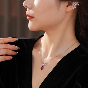 Detail of silver necklace with red teardrop gemstone and floral tassel ear cuff set