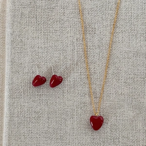 Elegant gold necklace and heart earrings set with red stones on a linen backdrop