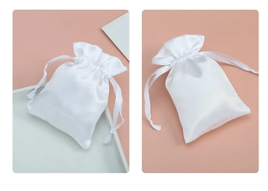 Close-up of white satin drawstring jewelry pouch with smooth glossy texture and ribbon
