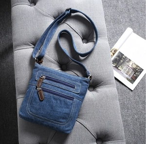 Detail of blue denim crossbody bag featuring multiple zipper pockets on a gray surface