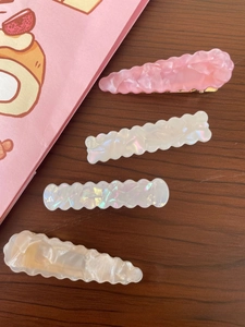 Detail view of four acetic acid hair clips in pink and pearl white with marble textures