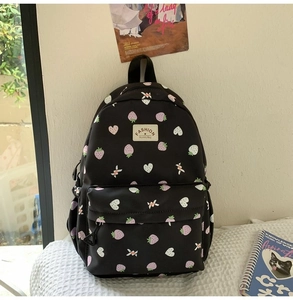 Detail of cute strawberry and heart print on black nylon school backpack with fashion label