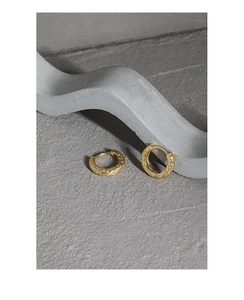 Detailed view of gold huggie earrings with a hammered texture on a gray stone surface