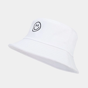 Détail d'un bob en coton blanc avec un motif de smiley brodé en noir sur le côté