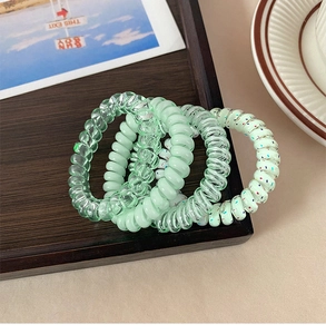 Detailed view of four green spiral hair ties on a wooden tray with a decorative card