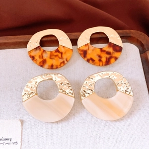 Detail of round hollow resin earrings in tortoiseshell and cream with golden metal finish