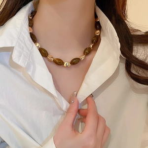 Detail of resin oval brown and irregular gold beads on a classic necklace worn by model