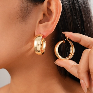 Detailed view of thick gold hoop earrings showing the latch mechanism and width on a model