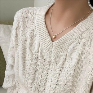 Close-up of a minimalist gold heart pendant necklace worn on a cozy white knit sweater