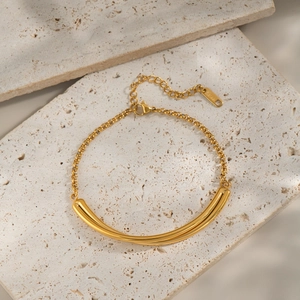 Minimalist double-tube curved gold titanium steel bracelet on beige travertine stone