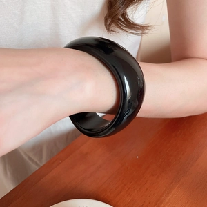 Close-up of a wide black resin geometric open bangle worn on a female wrist
