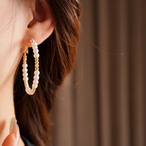 Detail of beaded pearl hoop earrings on model with golden engraved metal accents