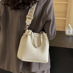 Chic cream leather bucket bag with a patterned wide shoulder strap and gold hardware accents