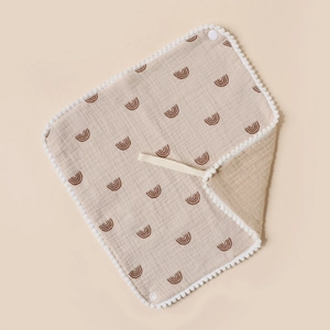 Detailed macro view of cotton baby bib with rainbow print and fluffy white pom-pom edges