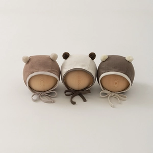 Soft knitted baby earflap hats in beige, cream, and brown with fluffy pom-poms