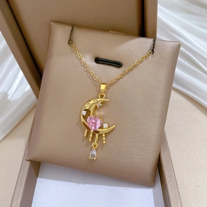 Close-up of golden moon pendant with pink heart gemstone on a brown velvet stand