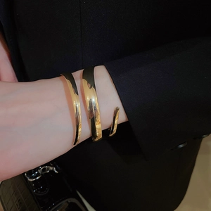 Close-up of a wide polished gold wrap-around cuff bracelet on a female model's arm