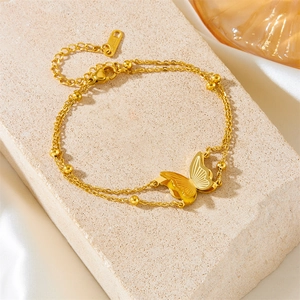 Detail of double-layer gold chain bracelet with butterfly charm and small beads on stone