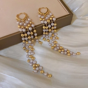 Macro detail of elegant long tassel earrings with white pearls on a soft silk background